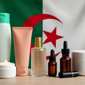 Une variété de produits cosmétiques (shampoing, crème, parfum, sérums, rouge à lèvres) présentée avec le drapeau algérien en arrière-plan.
